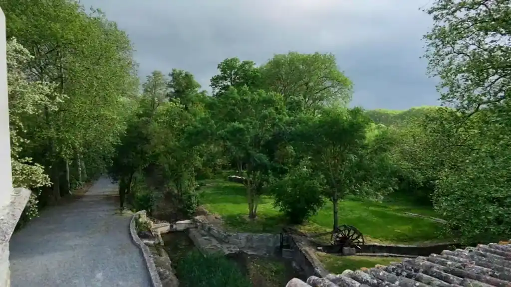 Gefilmd met een drone: over de dakrand naar de tuin, met de stenen goot, het ijzeren rad en de bomen.